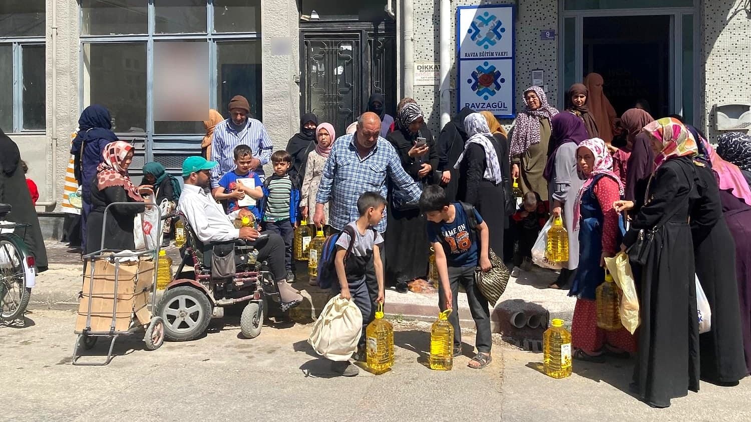 Vakıf binasının önünde dağıtım gününde sıraya giren aileler ve yerde duran ayçiçek yağı bidonları