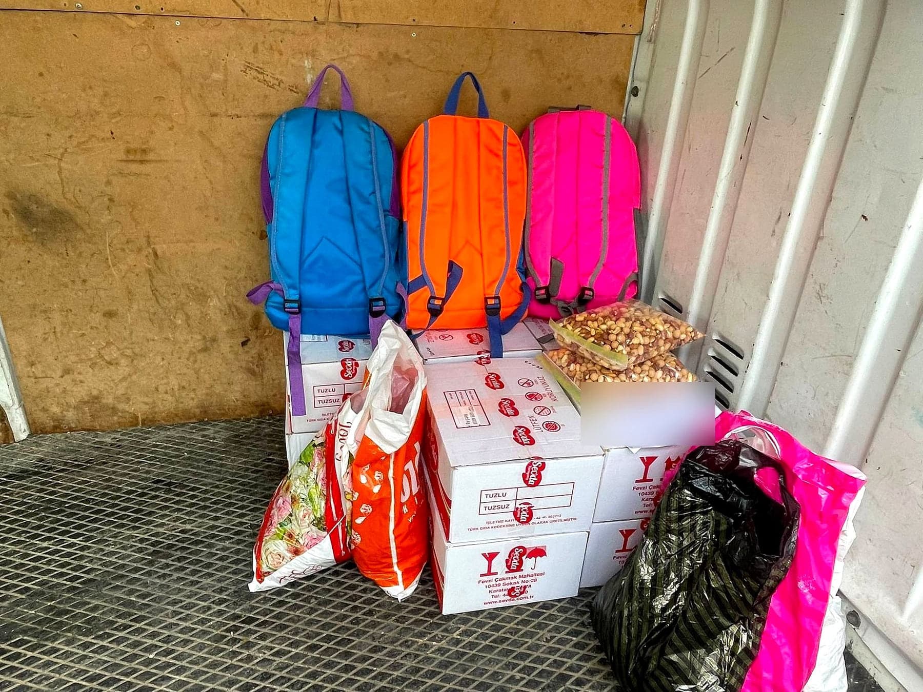 Dağıtıma hazırlanmış üç okul çantası, gıda kolileri ve bakliyat paketleri