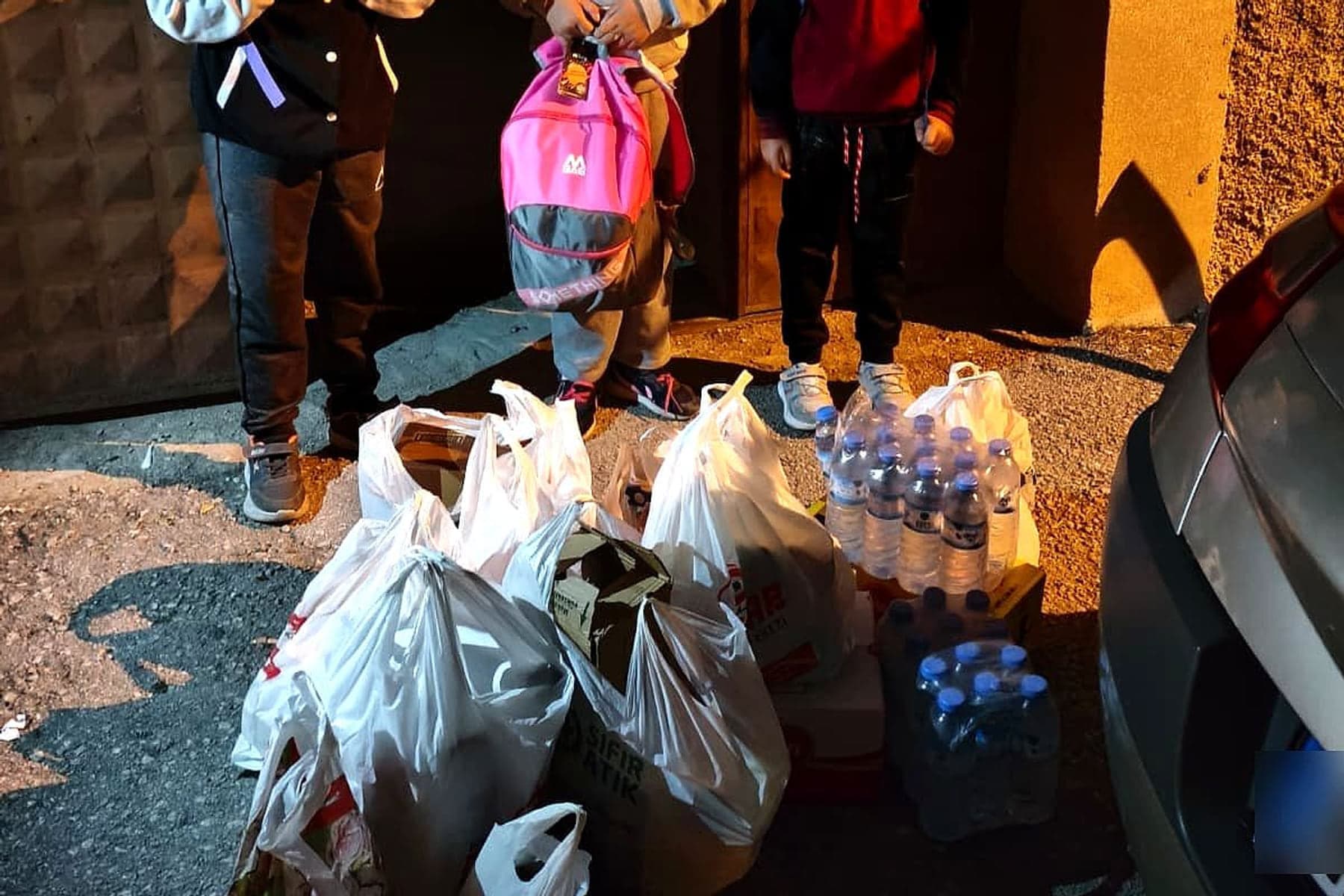 Bir evin kapısı önünde teslim edilen gıda poşetleri, su ve okul çantası